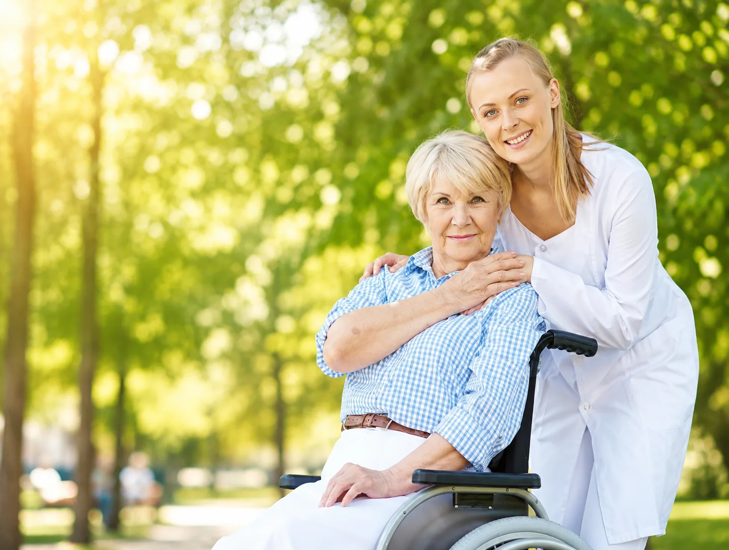 Nurse in a white coat accompanying a senior woman in a wheelchair outdoors